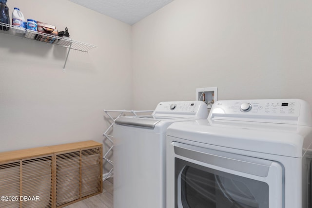 laundry room featuring light wood-style floors, washing machine and dryer, laundry area, and a textured ceiling