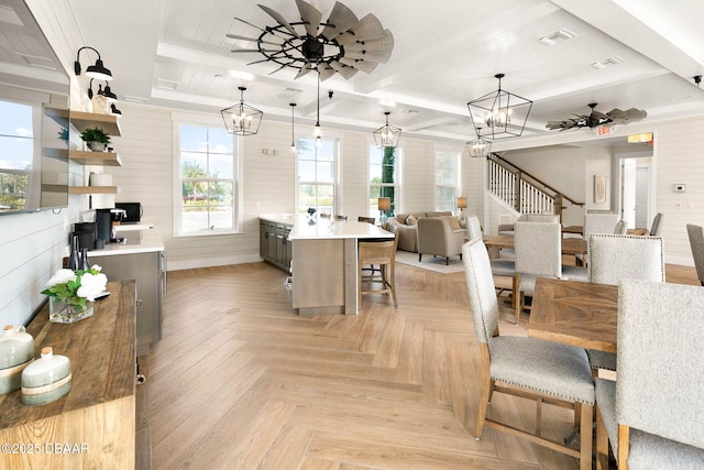 dining room with stairway, a healthy amount of sunlight, wooden walls, and ceiling fan with notable chandelier