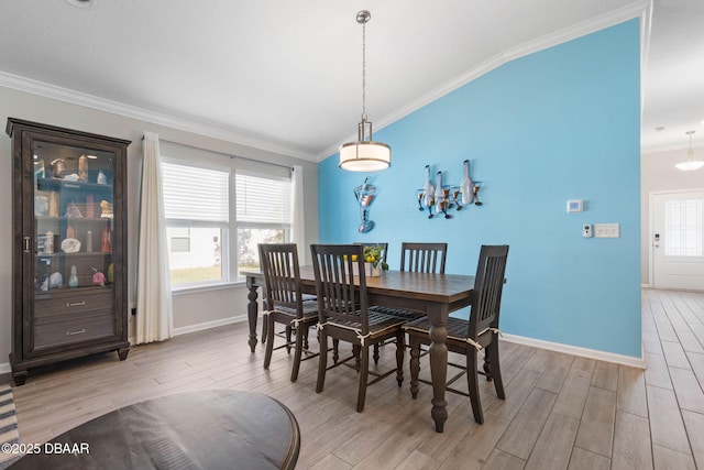 dining area featuring crown molding, baseboards, lofted ceiling, and light wood-style floors