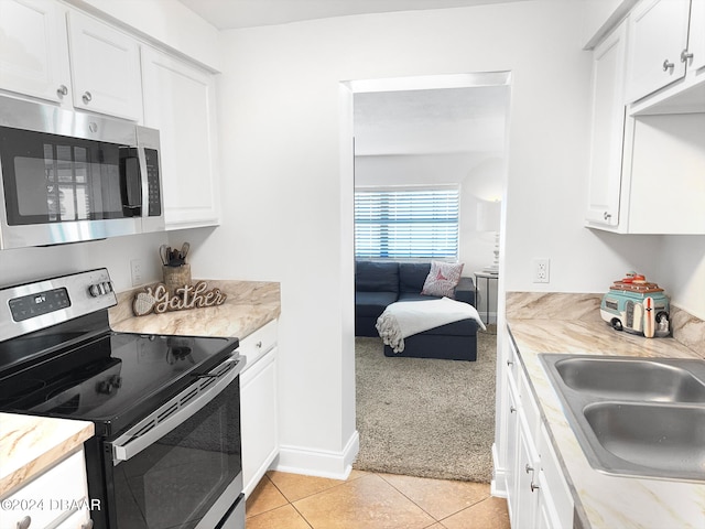 kitchen with sink, light stone counters, appliances with stainless steel finishes, white cabinets, and light colored carpet