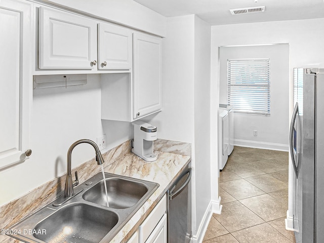 kitchen featuring stainless steel appliances, sink, light tile patterned flooring, white cabinetry, and washing machine and dryer