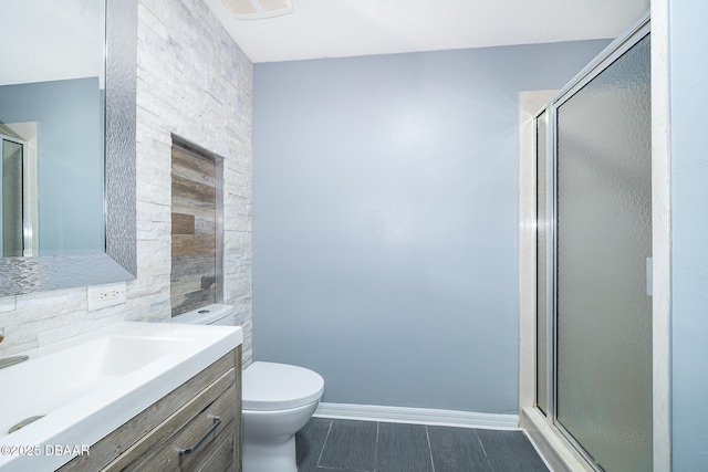 bathroom featuring toilet, vanity, decorative backsplash, and a shower with shower door