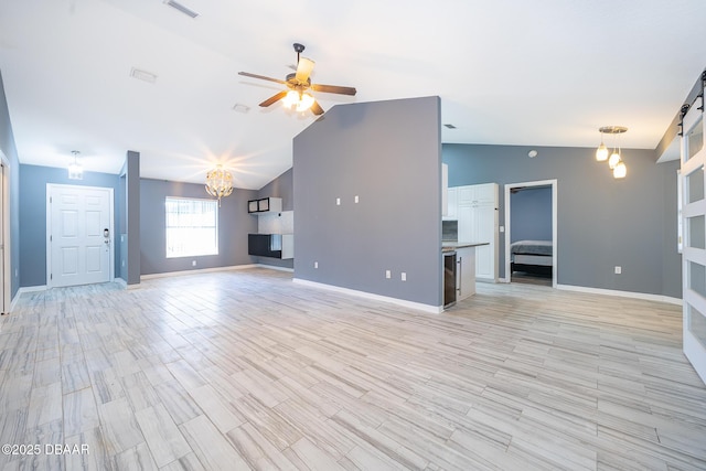 unfurnished living room featuring ceiling fan with notable chandelier, vaulted ceiling, and light hardwood / wood-style flooring