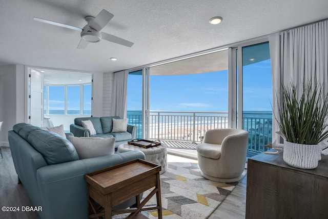 living room featuring ceiling fan, floor to ceiling windows, a water view, and light wood-type flooring