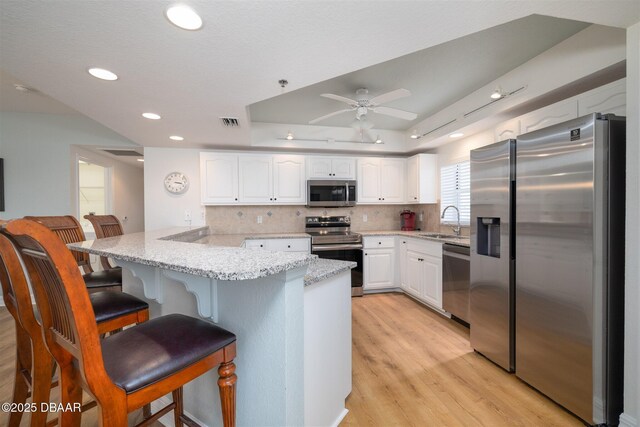 kitchen featuring kitchen peninsula, ceiling fan, light stone countertops, appliances with stainless steel finishes, and white cabinetry