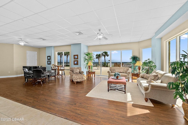 living area with visible vents, a ceiling fan, a drop ceiling, wood finished floors, and baseboards