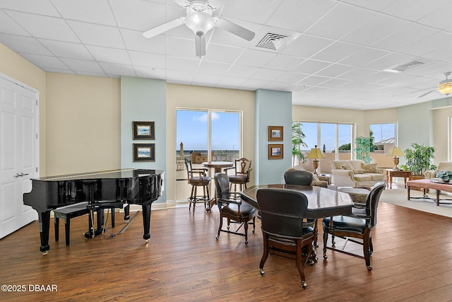 dining area with dark wood-style floors, visible vents, ceiling fan, and a drop ceiling