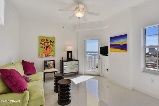 living area with tile patterned flooring, crown molding, a ceiling fan, and baseboards