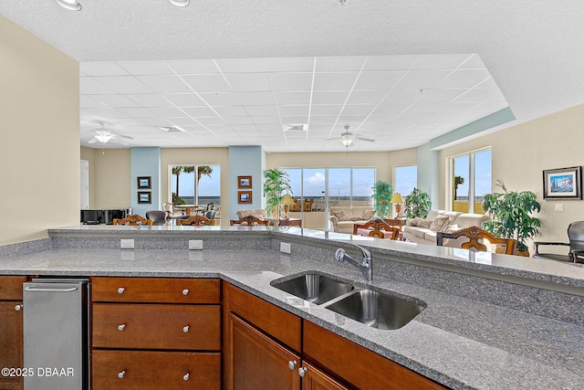 kitchen with visible vents, open floor plan, brown cabinetry, a ceiling fan, and a sink