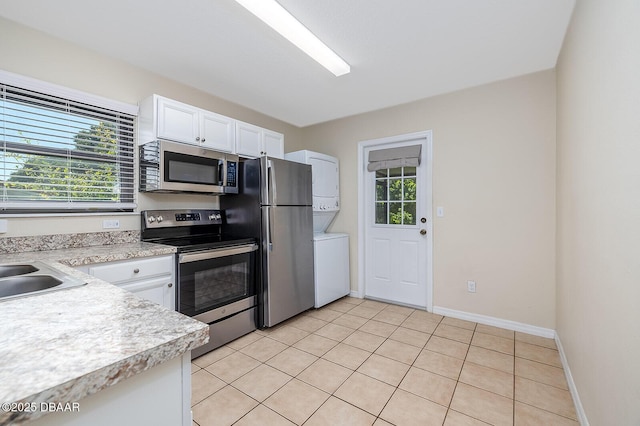 59 Cardinal Dr Unit A, Ormond Beach, FL 32176 - kitchen with appliances with stainless steel finishes, estacked washer and dryer, light countertops, white cabinets, and light tile patterned flooring