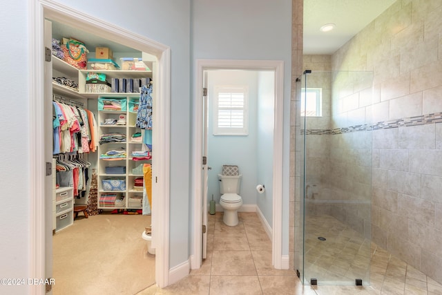 full bath featuring tile patterned flooring, a spacious closet, toilet, baseboards, and a shower stall