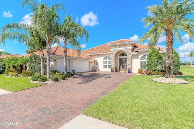 mediterranean / spanish house with a tiled roof, decorative driveway, a garage, a front lawn, and stucco siding