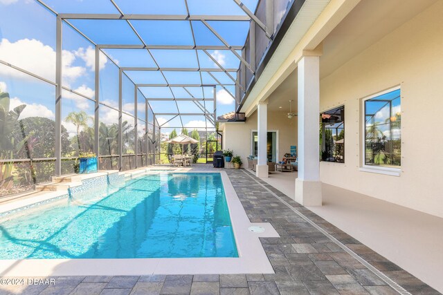 outdoor pool with glass enclosure, ceiling fan, and a patio area