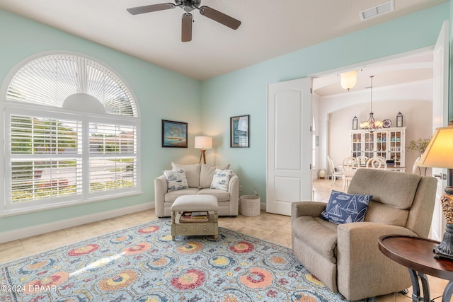 tiled living area featuring ceiling fan with notable chandelier, visible vents, and baseboards