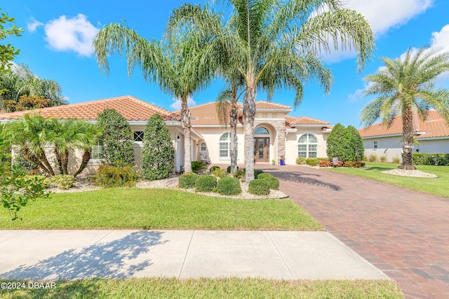 mediterranean / spanish-style home featuring stucco siding, a tile roof, a front lawn, and decorative driveway