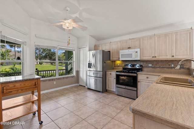 kitchen with appliances with stainless steel finishes, sink, vaulted ceiling, and light tile patterned floors