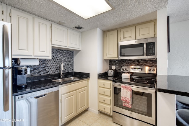 kitchen featuring backsplash, appliances with stainless steel finishes, a textured ceiling, light tile patterned floors, and sink