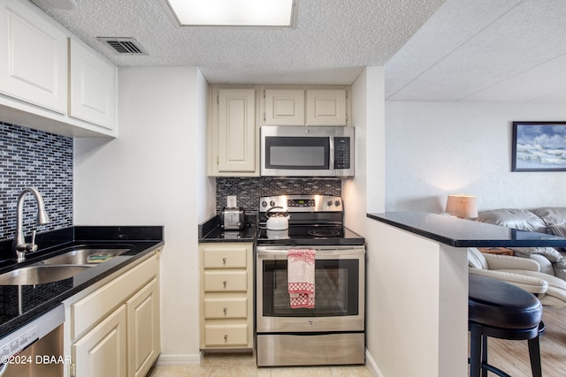 kitchen featuring tasteful backsplash, stainless steel appliances, a textured ceiling, sink, and a kitchen breakfast bar