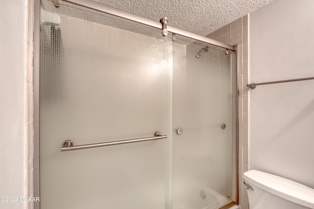 bathroom featuring walk in shower, toilet, and a textured ceiling