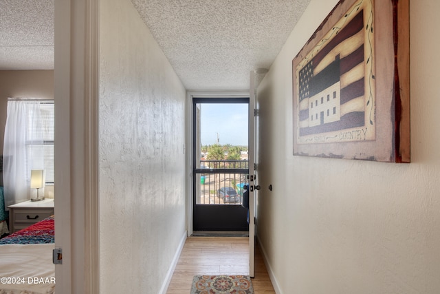 hall featuring light wood-type flooring, a wealth of natural light, and a textured ceiling