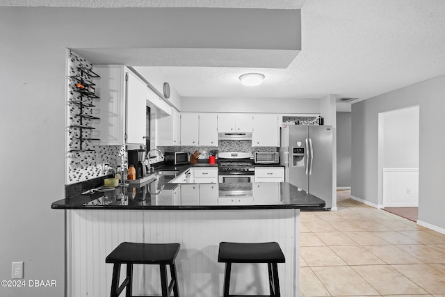 kitchen with backsplash, white cabinets, a kitchen bar, kitchen peninsula, and stainless steel appliances