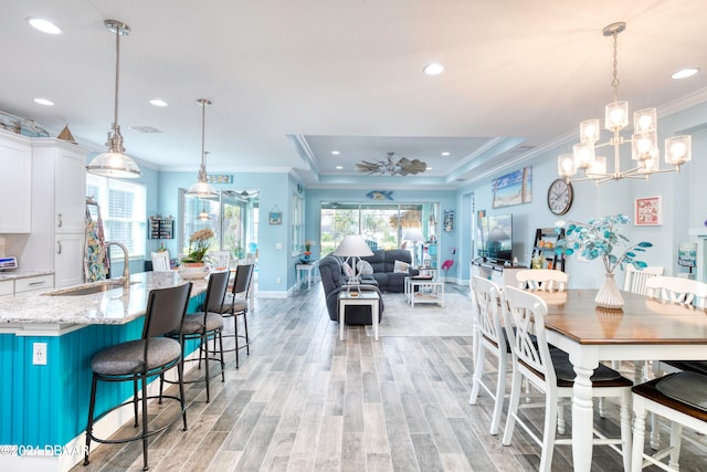 dining room featuring sink, a raised ceiling, light hardwood / wood-style flooring, crown molding, and a notable chandelier