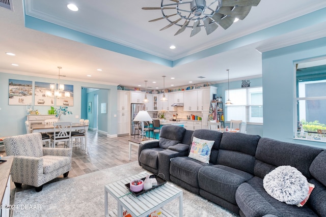 living room featuring ceiling fan with notable chandelier, light hardwood / wood-style floors, crown molding, and a tray ceiling