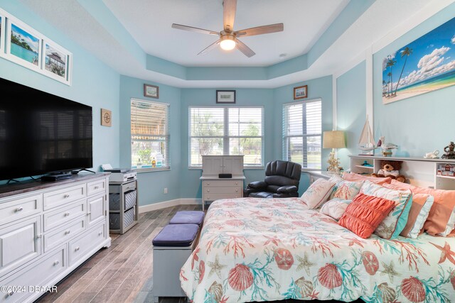 bedroom with a tray ceiling, ceiling fan, and light hardwood / wood-style flooring