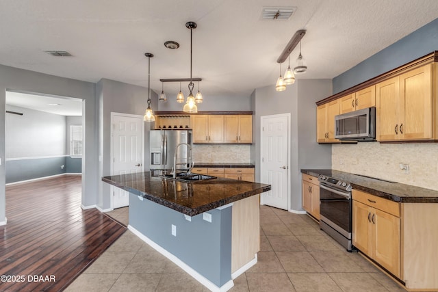 kitchen featuring a kitchen island with sink, backsplash, light tile patterned floors, and stainless steel appliances