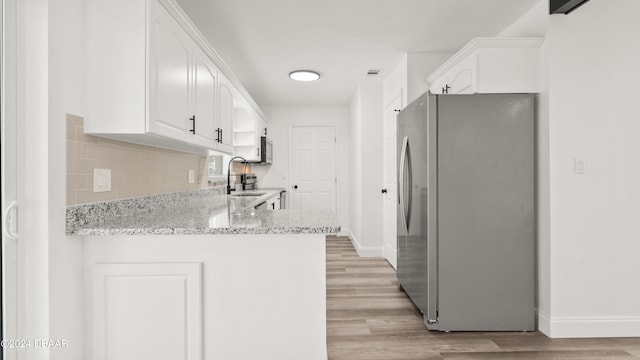 kitchen featuring white cabinetry, kitchen peninsula, appliances with stainless steel finishes, light stone countertops, and light wood-type flooring