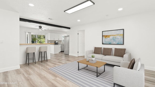 living room featuring beam ceiling, a textured ceiling, ceiling fan, and light hardwood / wood-style flooring