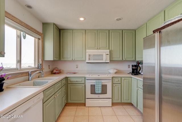 kitchen featuring light tile patterned floors, light countertops, green cabinets, a sink, and white appliances