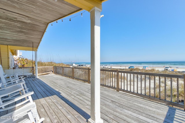 wooden terrace featuring a beach view and a water view