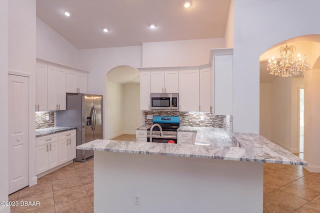 kitchen with kitchen peninsula, appliances with stainless steel finishes, white cabinets, and tasteful backsplash