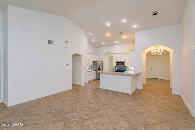 kitchen with high vaulted ceiling, an inviting chandelier, white cabinets, light stone countertops, and appliances with stainless steel finishes