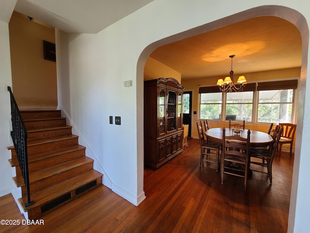 dining room featuring dark wood-style floors, arched walkways, baseboards, a chandelier, and stairs