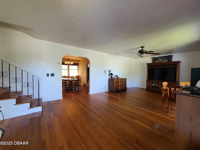 unfurnished living room with arched walkways, ceiling fan with notable chandelier, stairs, and hardwood / wood-style flooring