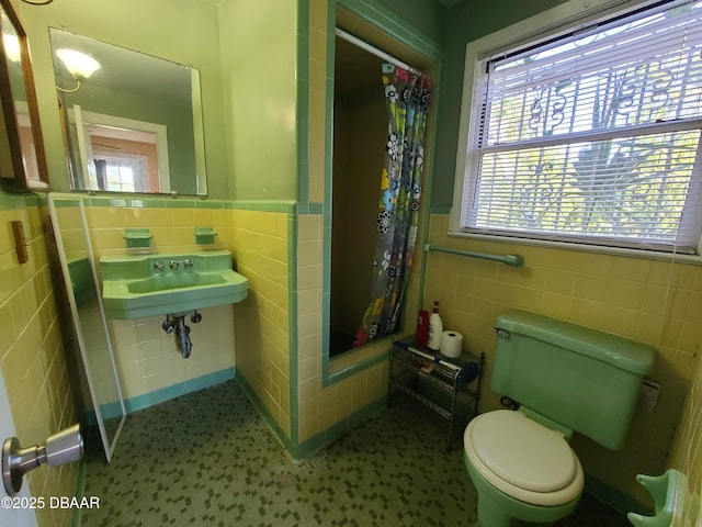 bathroom with a shower stall, toilet, wainscoting, tile walls, and a sink