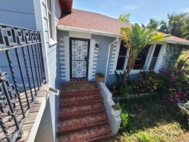 view of exterior entry featuring stone siding and roof with shingles