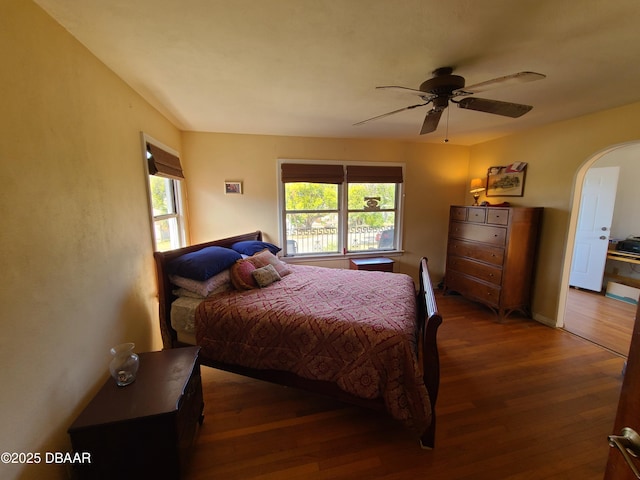 bedroom with arched walkways, wood finished floors, and a ceiling fan