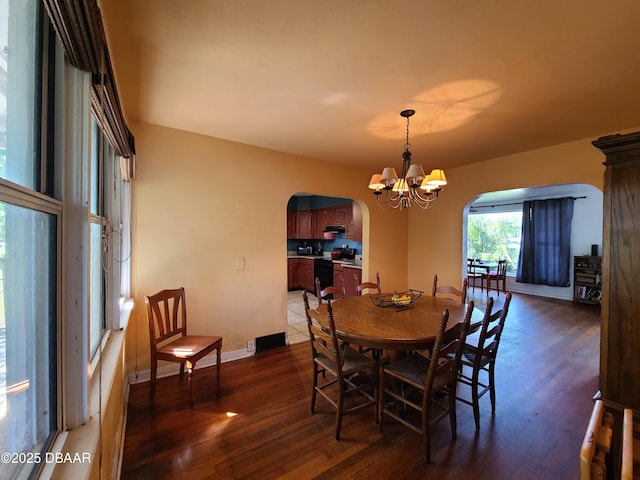 dining space with baseboards, wood finished floors, arched walkways, and a chandelier