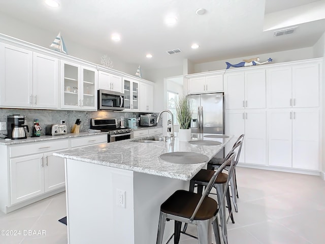 kitchen featuring a center island with sink, backsplash, white cabinetry, and stainless steel appliances