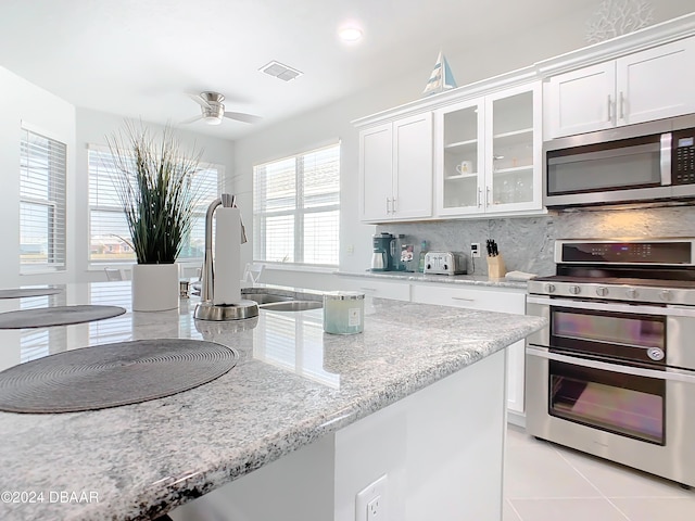 kitchen featuring white cabinets, decorative backsplash, stainless steel appliances, and ceiling fan