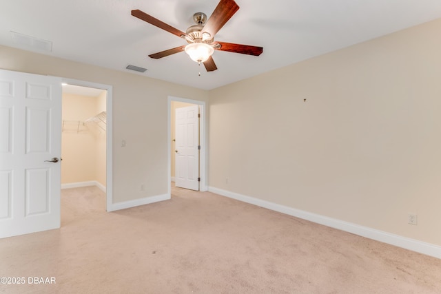 unfurnished bedroom featuring visible vents, light carpet, a walk in closet, a closet, and baseboards