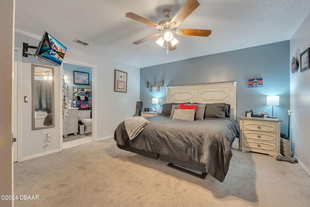 bedroom with ceiling fan, light colored carpet, a textured ceiling, and connected bathroom