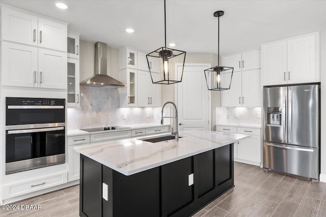 kitchen with stainless steel appliances, a center island with sink, sink, white cabinetry, and wall chimney exhaust hood