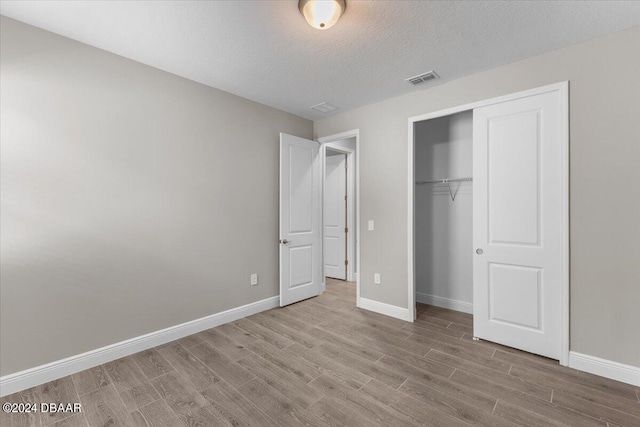 unfurnished bedroom with light hardwood / wood-style flooring, a textured ceiling, and a closet