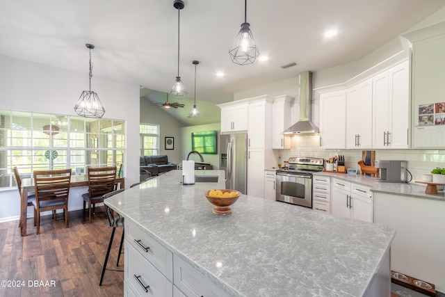 kitchen featuring wall chimney range hood, white cabinets, hanging light fixtures, and stainless steel appliances