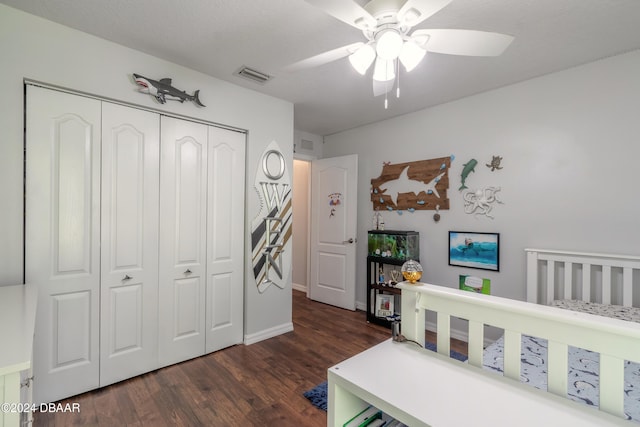 bedroom featuring a nursery area, dark wood-type flooring, ceiling fan, and a closet