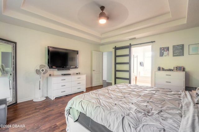 bedroom featuring dark hardwood / wood-style floors, ceiling fan, a tray ceiling, a barn door, and connected bathroom